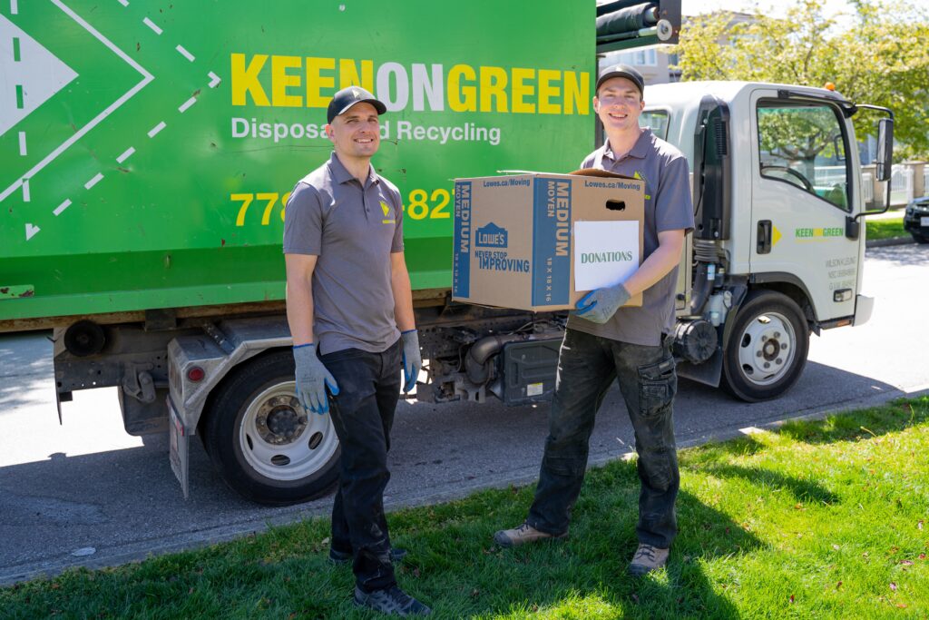 Eco-Friendly Junk Removal - two young men in uniform carrying a box with a junk removal truck in the background.